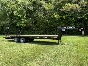 For sale in Ohio: a 20k Tandem Dual Gooseneck Trailer branded Advanced. This dual axle flatbed, surrounded by dense trees and resting on grass, features rear loading ramps.