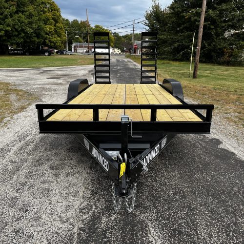 The 10k Equipment Trailer with a wooden deck is parked in Ohio. It has double rear ramps and side branding, set against trees and buildings under a cloudy sky, creating an appealing trailer for sale.