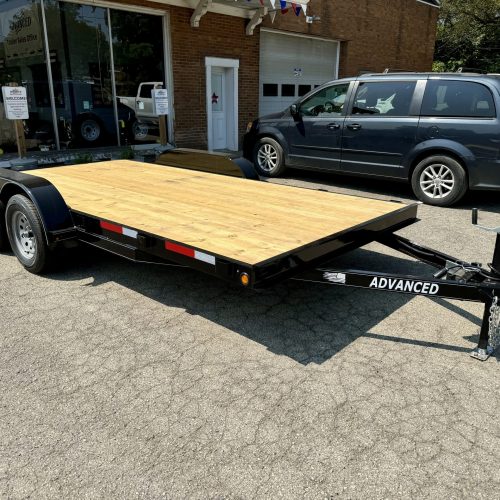 A 7k Single Car Trailer with a wooden platform and dual axles is parked outside an Ohio building. The black frame reads ADVANCED. Nearby, a minivan is positioned in front of a brick building with large windows.