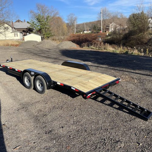 A 10k Single Car Trailer with dual axles is available in Ohio. It has a wooden deck and a foldable metal ramp, parked on gravel against a backdrop of trees, houses, and clear blue sky.