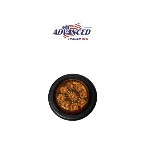 The 2 LED Light, a circular amber LED with black casing and eight smaller surrounding lights, displays the Advanced Trailer MFG logo with an American flag on a white backdrop. Ideal for Ohio trailer buyers, it offers enhanced visibility and style.