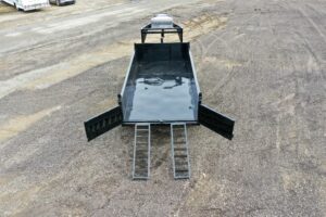 A 14K Gooseneck Low Profile Dump Trailer in black is shown from above with rear doors open and two metal loading ramps extended onto a gravel surface.