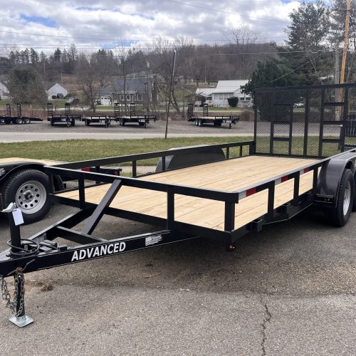 A 16 Tandem Axle Utility Trailer with a wooden deck and metal frame, featuring a rear ramp and ADVANCED branding, is parked outdoors. Other trailers and trees are visible in the background.