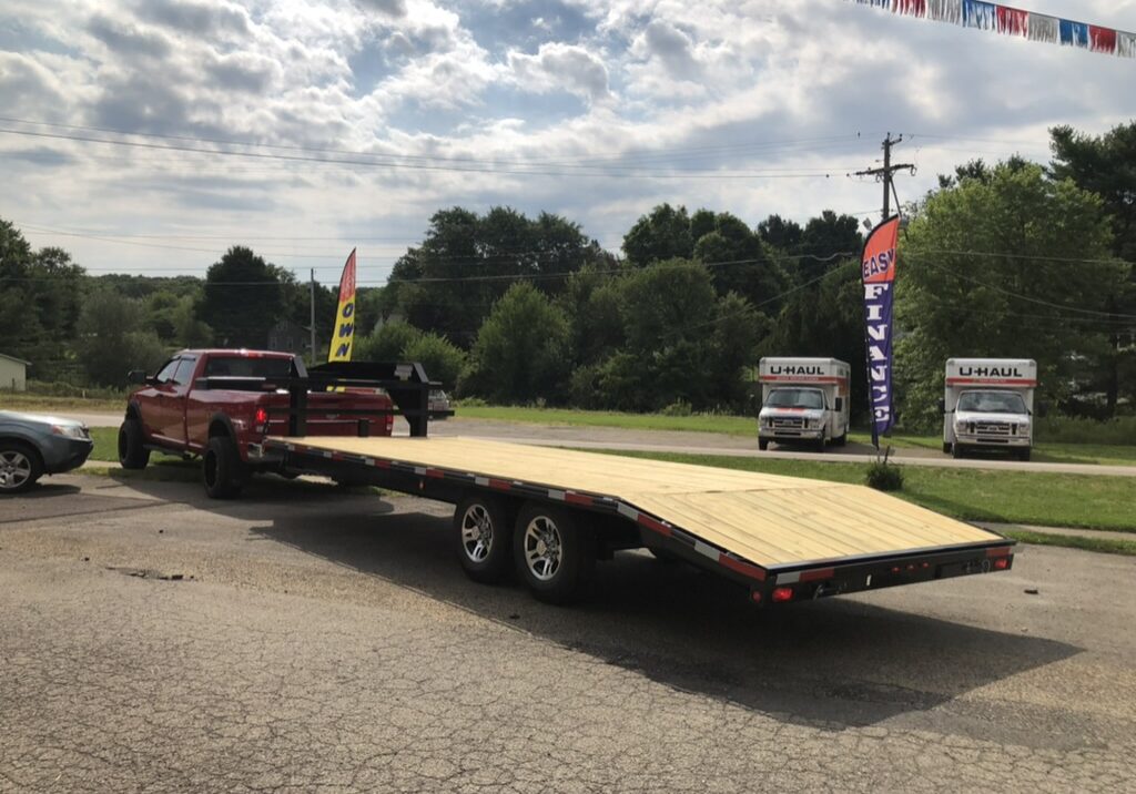 A red truck with a flatbed trailer is parked on a paved lot in Ohio under a cloudy sky. Nearby, two U-Haul trucks are stationed. Flags and trees lend color to the scene, enhancing the subtle charm of this trailer for sale setting. A red truck with a flatbed trailer is parked on a paved lot in Ohio under a cloudy sky. Nearby, two U-Haul trucks are stationed. Flags and trees lend color to the scene, enhancing the subtle charm of this trailer for sale setting.