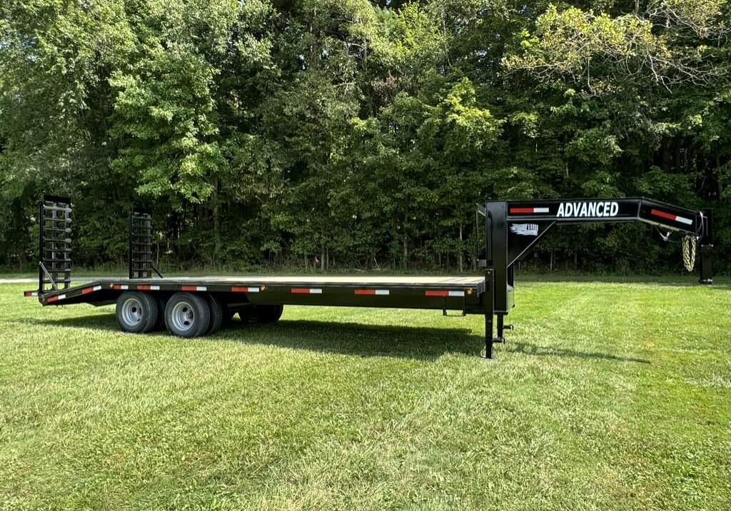 For sale in Ohio: a 20k Tandem Dual Gooseneck Trailer branded Advanced. This dual axle flatbed, surrounded by dense trees and resting on grass, features rear loading ramps. For sale in Ohio: a 20k Tandem Dual Gooseneck Trailer branded Advanced. This dual axle flatbed, surrounded by dense trees and resting on grass, features rear loading ramps.